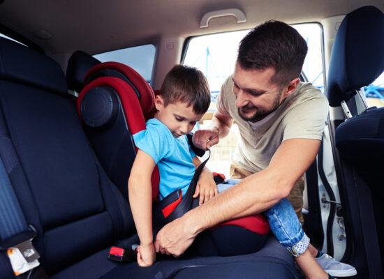Close-up shot of concentrated father helping his son to fasten belt on car seat