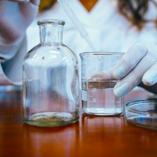 A scientist in a white lab coat testing water for PFAS contamination in various beakers