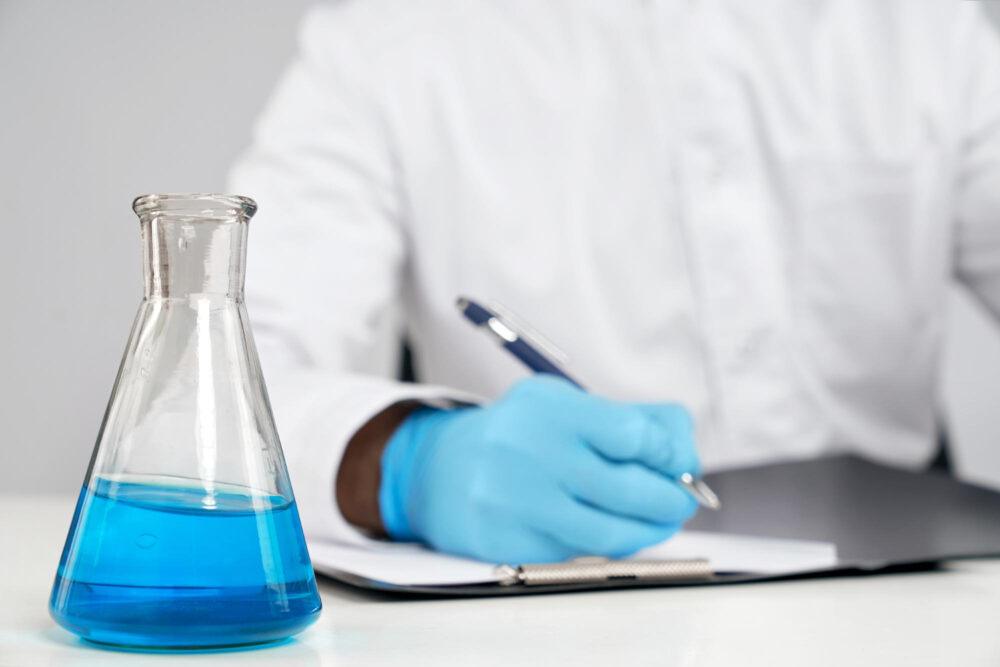 a scientist writing down information and studying a chemical in a vial