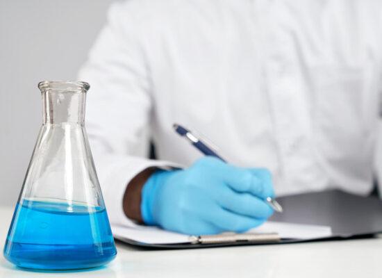 a scientist writing down information and studying a chemical in a vial