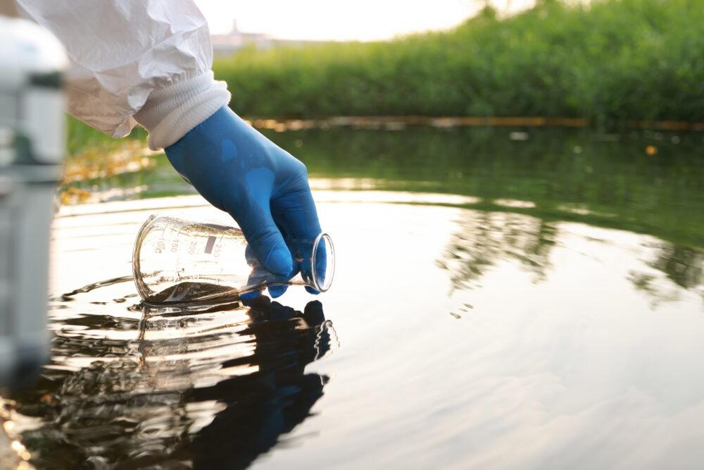 person in hazmat suit filling flask with pfas contaminated water