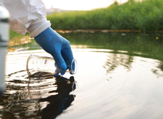 person in hazmat suit filling flask with pfas contaminated water