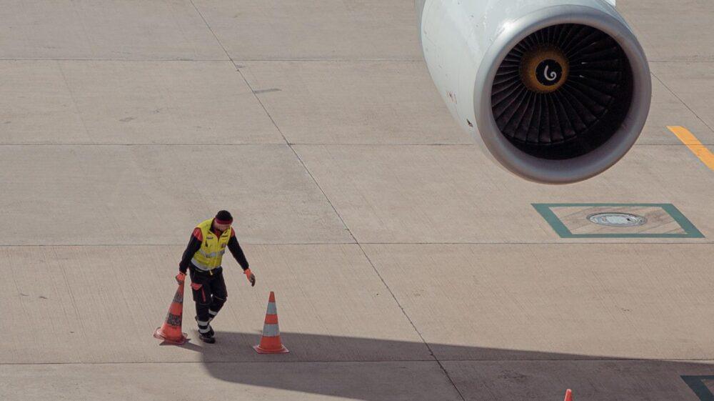 an airport worker picks up orange traffic cones on the tarmac near a parked airplane