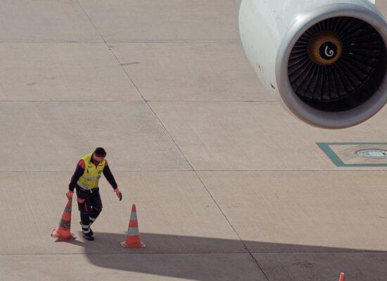 an airport worker picks up orange traffic cones on the tarmac near a parked airplane